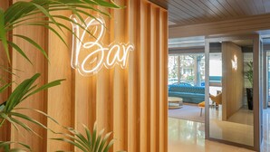 A wooden wall with a neon sign reading "Bar" and a glimpse of a modern interior with a blue sofa and a glass door. - HF Ala Sul (Porto)