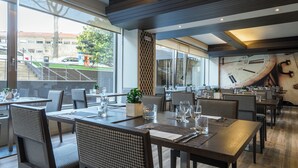 A modern restaurant with high ceilings, large windows, and a clock on the wall. Tables are set with glassware and napkins. - HF Ala Sul (Porto)