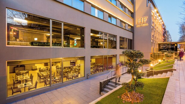 A modern hotel with multiple dining areas visible through large windows, a well-lit entrance, and a staircase leading to the upper floors. - HF Ala Sul (Porto)