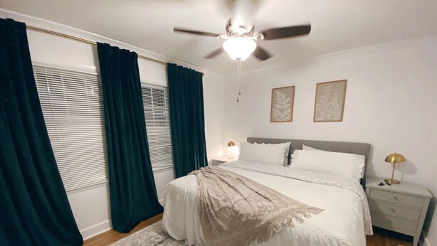 Ein Schlafzimmer mit einem Bett, einem Nachttisch, einem Deckenventilator und einem Fenster mit Vorhängen.