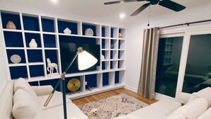 Ein modernes Wohnzimmer mit weißen Sofas, einer Stehlampe und einer blauen Regaleinheit mit Dekorationselementen.