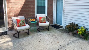 Eine Terrasse mit zwei Korbstühlen, einem kleinen Tisch mit einer Obstschale und Topfpflanzen.