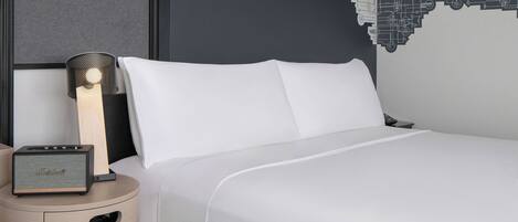 A neatly made bed with white linens, a lamp, and a speaker on a bedside table.