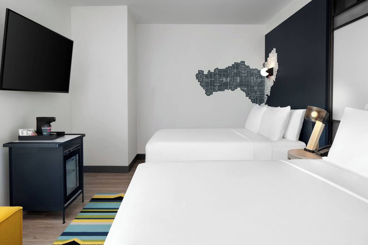 A modern hotel room with a large bed, a desk with a flat-screen TV, and a unique wall art piece.