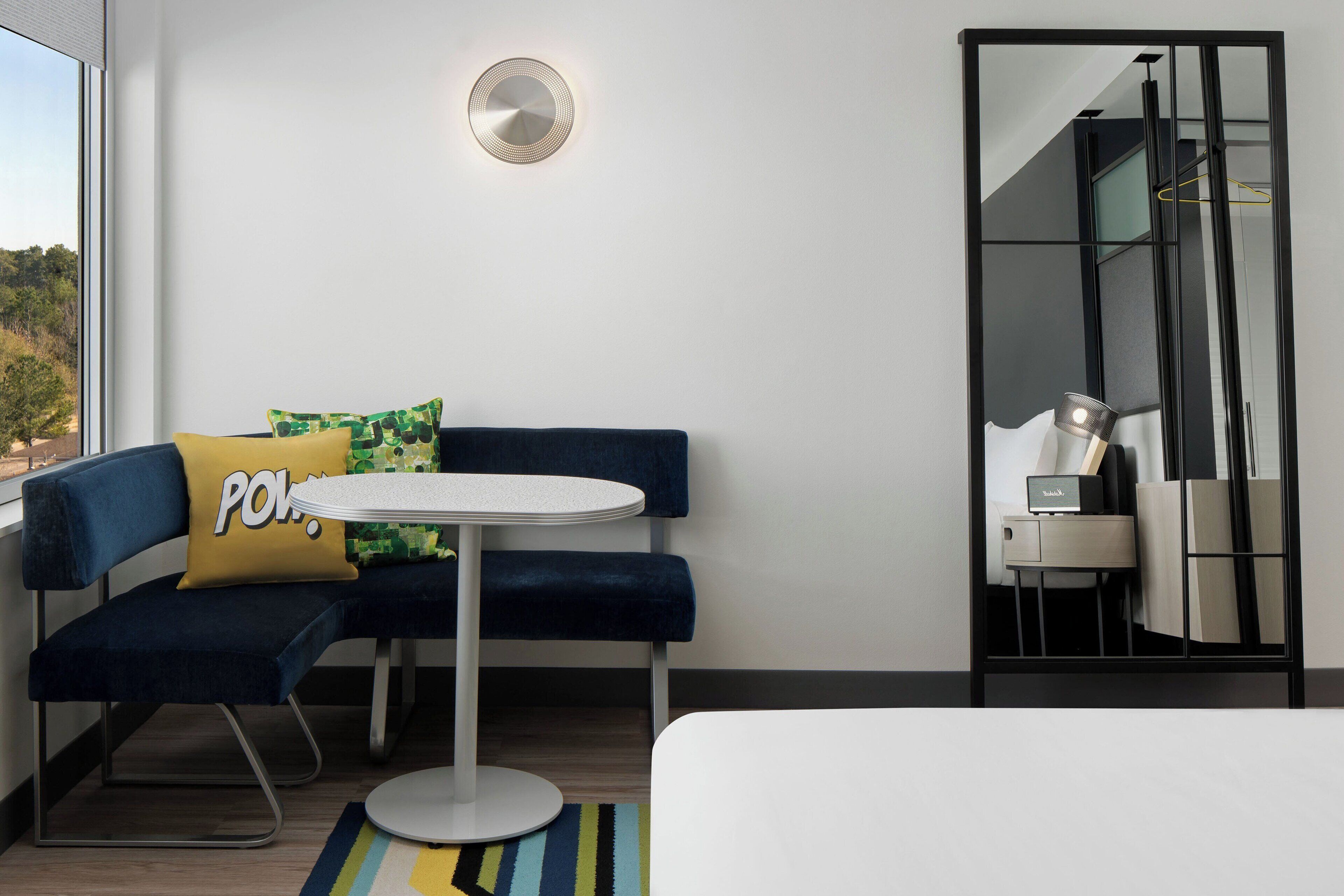 A modern hotel room with a blue sofa, a small round table, and a mirror.