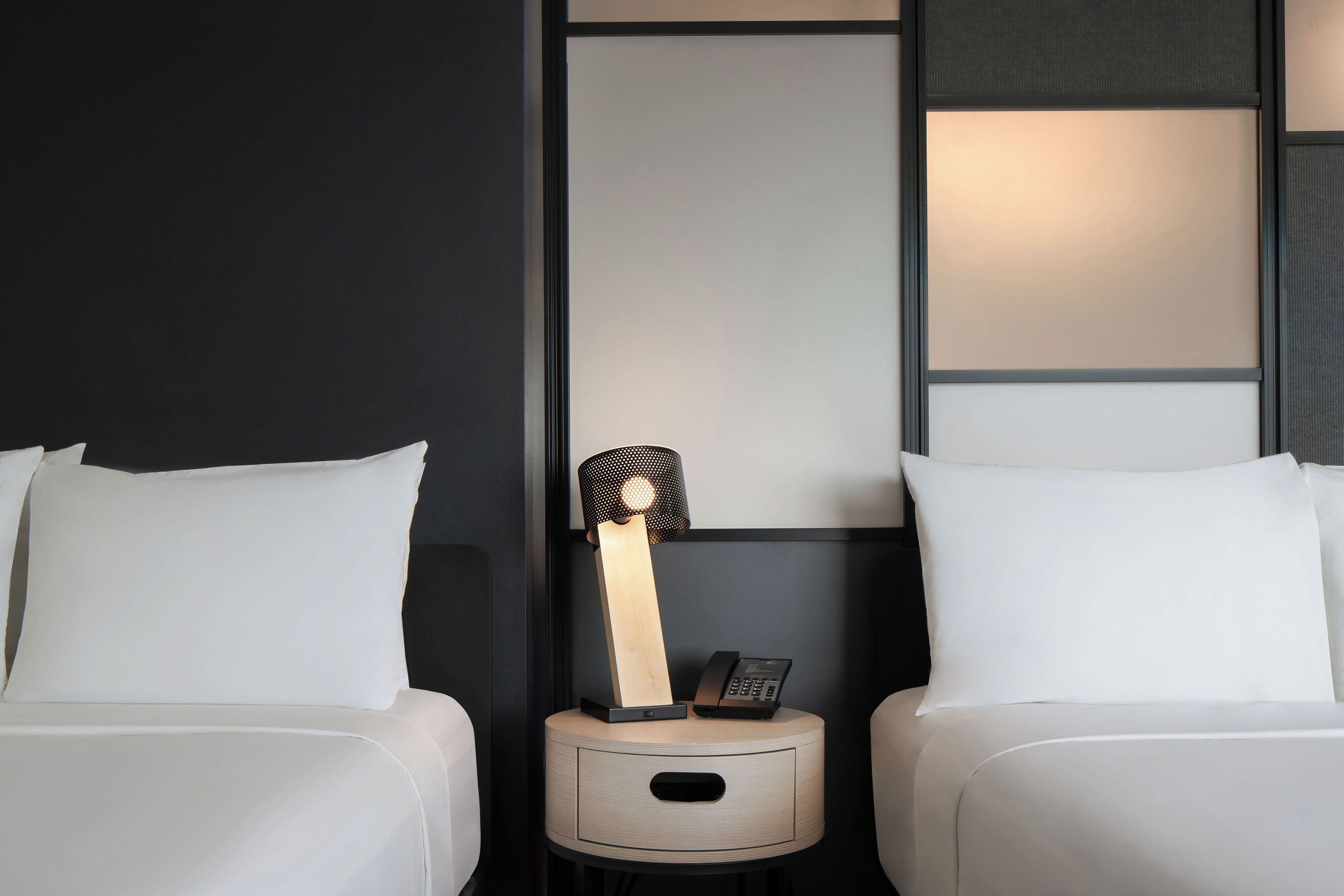 A hotel room with two beds, a nightstand with a lamp, and a telephone.