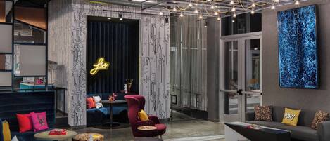 A modern lounge area with seating, a neon sign, and a large abstract painting.