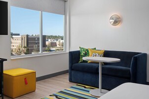 Una sala de estar moderna con un sofá azul, una mesita redonda pequeña y un otoman amarillo.