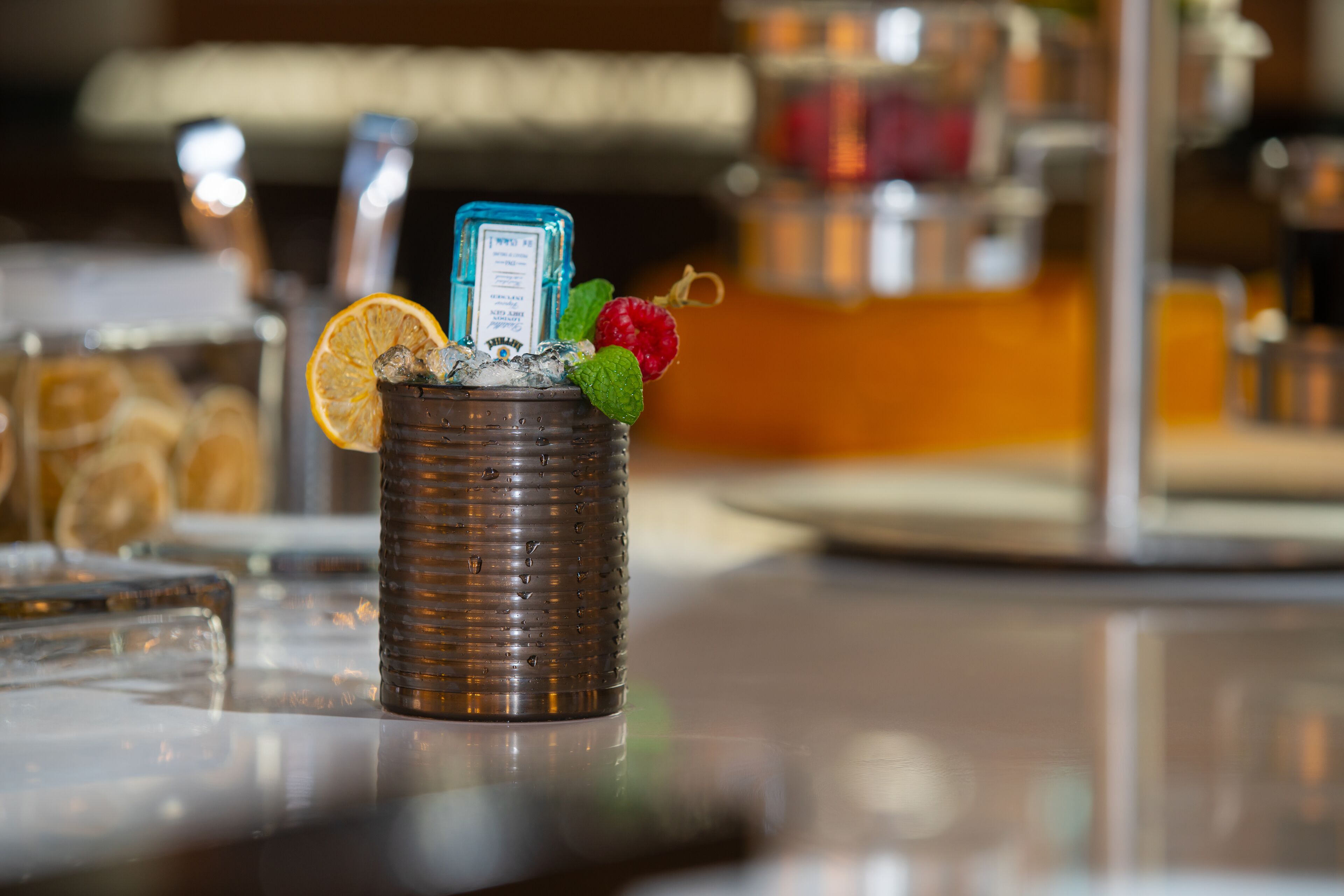 Un bar con una copa de cóctel que contiene hielo, una hoja de menta, una rodaja de naranja y una frambuesa.