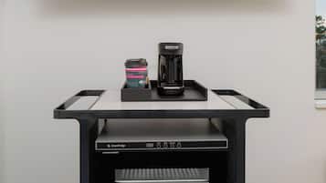 A coffee machine and a cup on a black tray table in front of a television.