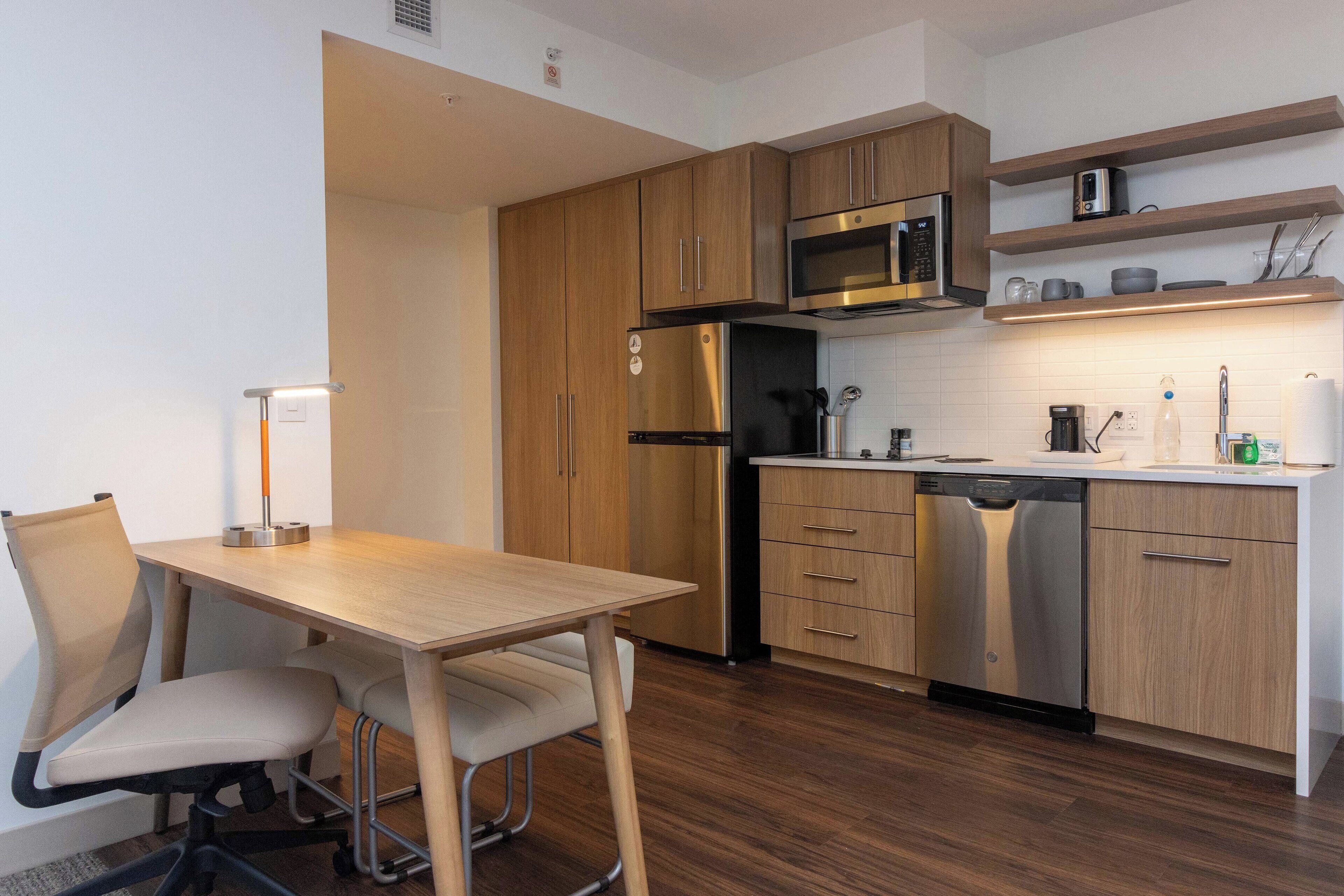 Una cocina moderna con armarios de madera, electrodomésticos de acero inoxidable, una mesa de comedor de madera con sillas y un estante empotrado para el microondas.