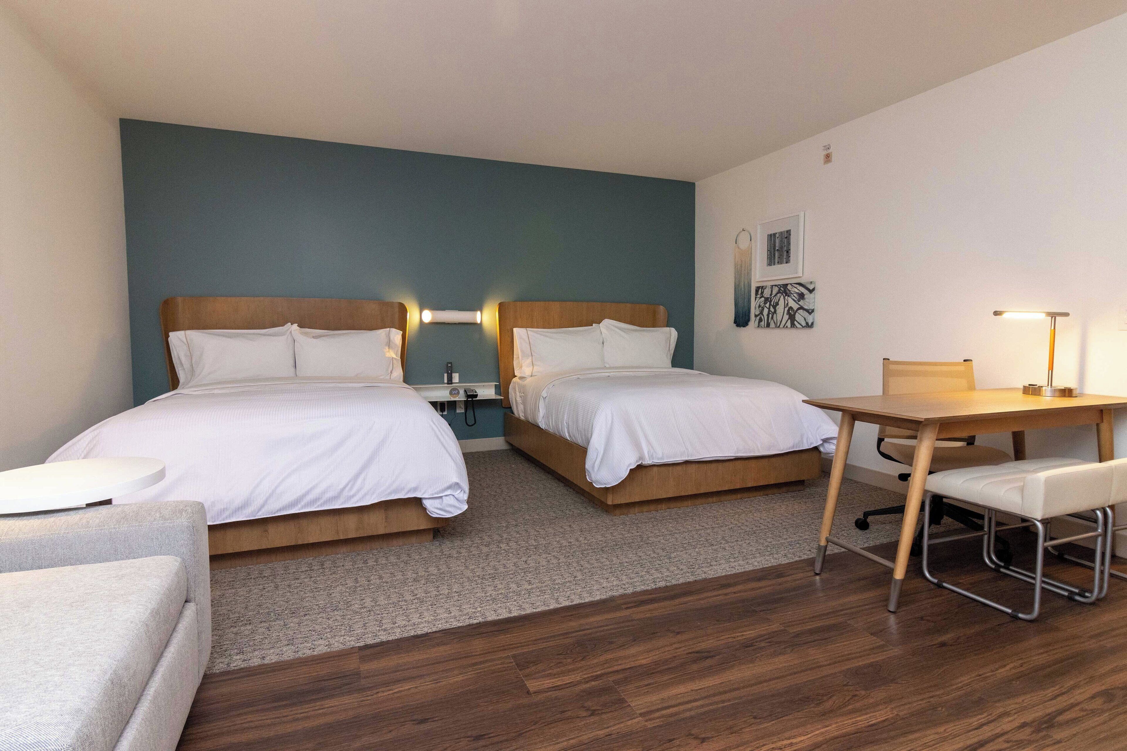 A hotel room with two beds, a desk, a chair, and a small table.