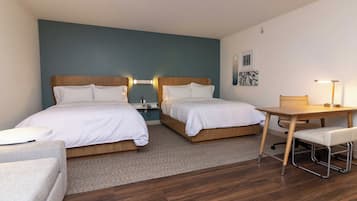 A hotel room with two beds, a desk, a chair, and a small table.