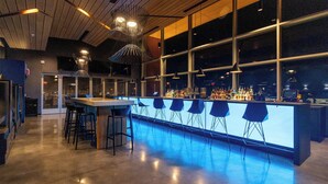 A modern bar area with a long counter, bar stools, and a variety of bottles.