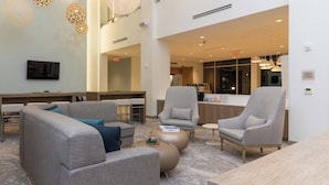 A modern hotel lobby with grey sofas, a coffee table, and a reception desk.