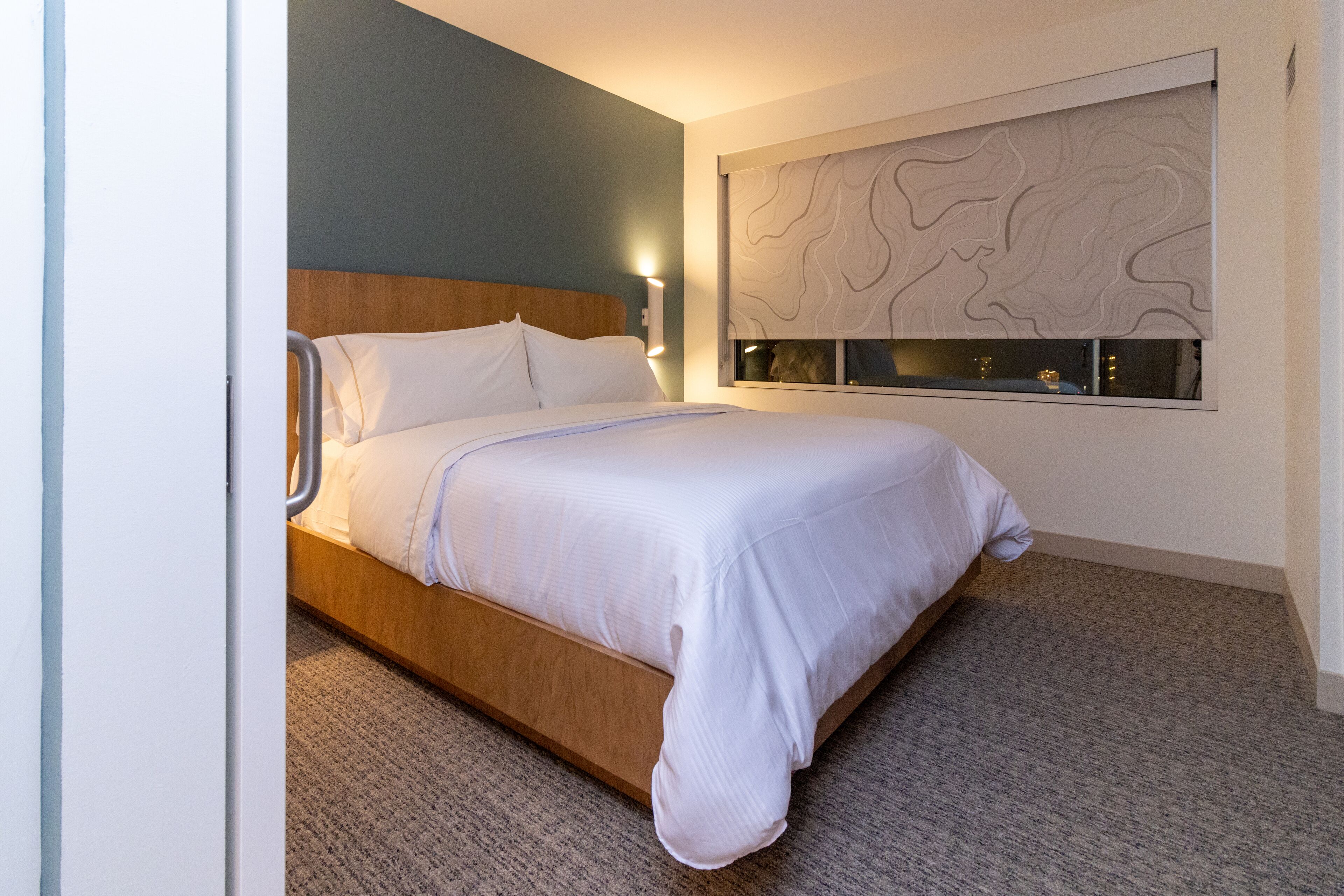 A modern hotel room with a wooden bed, a large wall-mounted artwork, and a carpeted floor.