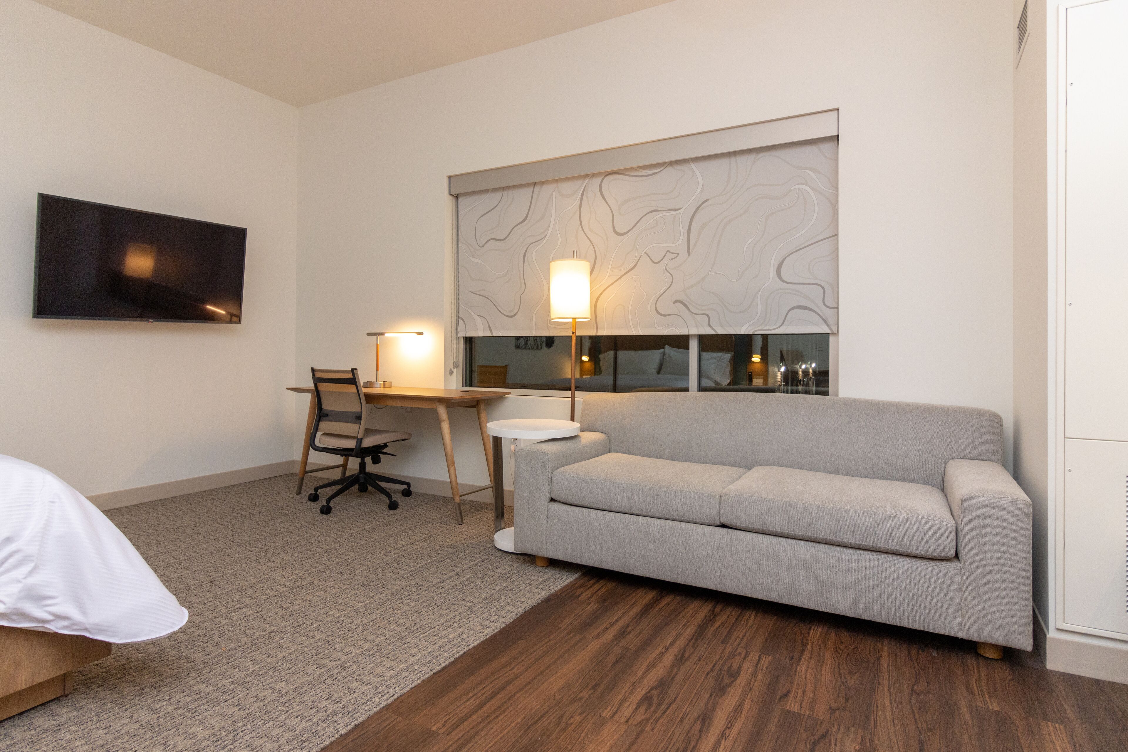 Una habitación de hotel moderna con televisión de pantalla plana, un sofá, un escritorio con silla y una lámpara.