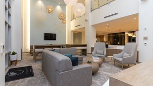 A spacious lobby with a modern design, featuring a seating area with sofas and armchairs, a reception desk, and a large window providing a view of the interior.