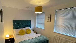 Een slaapkamer met een bed, nachtkastjes, een raam met zonwering en een radiator.