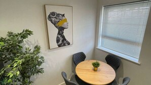 Een eetgedeelte met een ronde tafel, vier stoelen, een bloempot en een kunstwerk aan de muur.