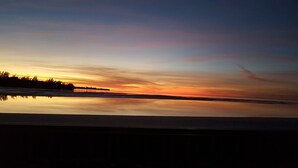 En stilla sjö som speglar en solnedgång, med silhuetten av träd synlig på vänster sida.