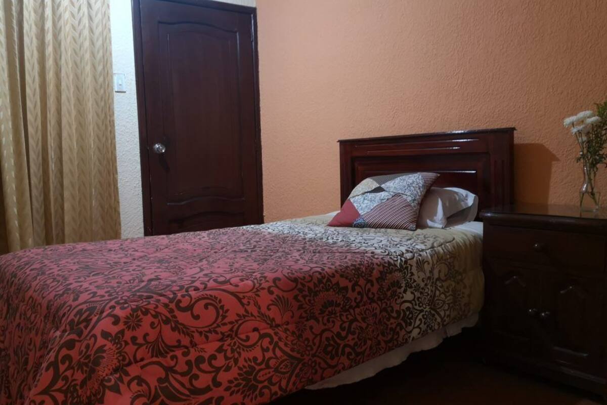 A bedroom with a bed, a wooden dresser, a door, and a curtain.
