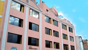 A pink hotel with multiple windows and a sign indicating a nearby road. - Hotel Rincon de la Alameda (Quito)