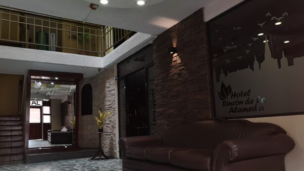 A lobby with a stone floor, a brown leather sofa, and a wall with a mural. - Hotel Rincon de la Alameda (Quito)
