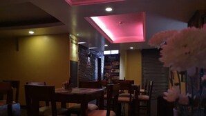 A dimly lit restaurant interior with wooden tables and chairs, a menu stand, and a wall with a menu board. - Hotel Rincon de la Alameda (Quito)