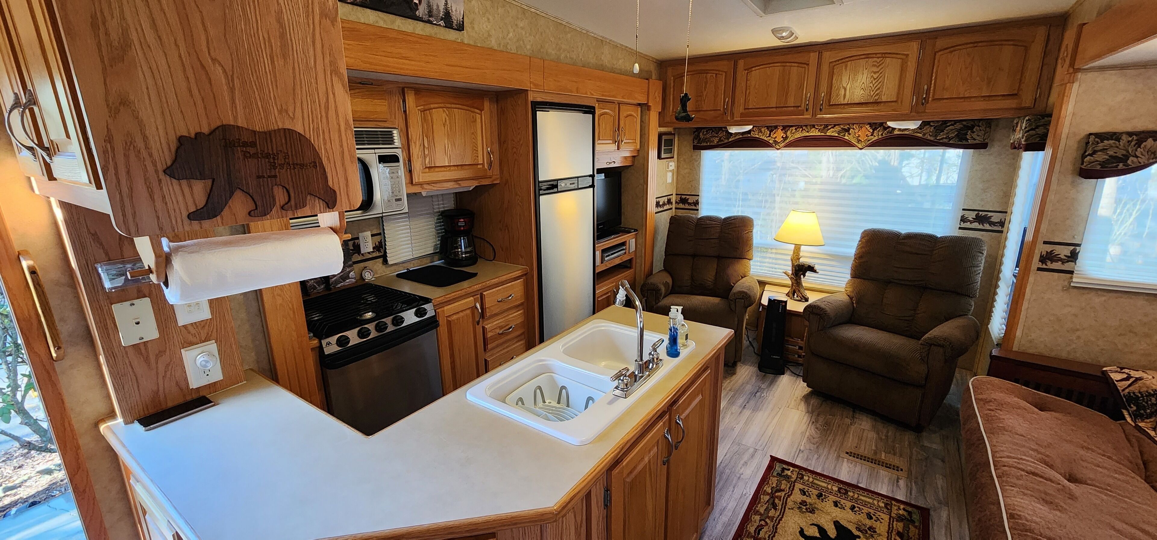 A compact RV kitchen with wooden cabinets, a stove, a sink, and a dining area with a chair and a table.