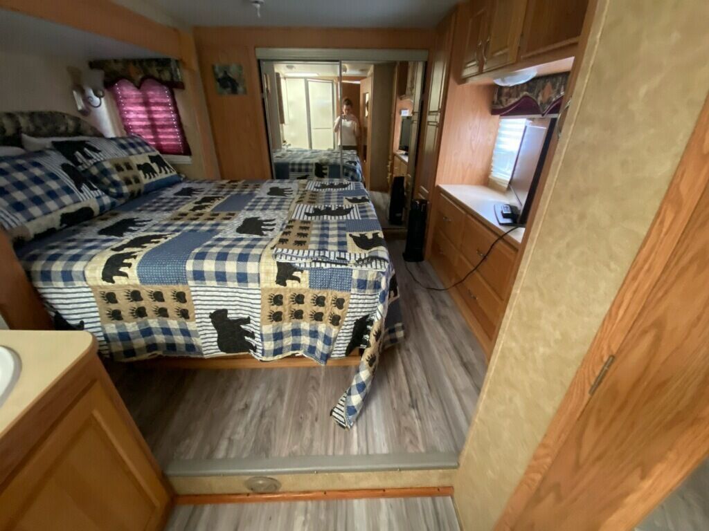 Ein kleines Schlafzimmer in einem Wohnmobil mit Bett, Schreibtisch und Fenster.