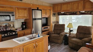 A compact RV kitchen with wooden cabinets, a stove, a sink, and a refrigerator. - Miss Daisy’s Retreat is a cozy getaway that will comfortably sleep four adults! (Gatlinburg)