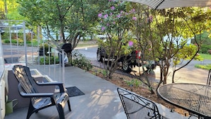 A covered outdoor seating area with a bench and a table, surrounded by trees and a parked vehicle. - Miss Daisy’s Retreat is a cozy getaway that will comfortably sleep four adults! (Gatlinburg)