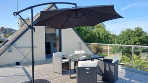 A deck with a table and chairs, an umbrella, and a view of greenery. - Bel appartement avec terrasse à 5mn de SAINT-CAST (Matignon)