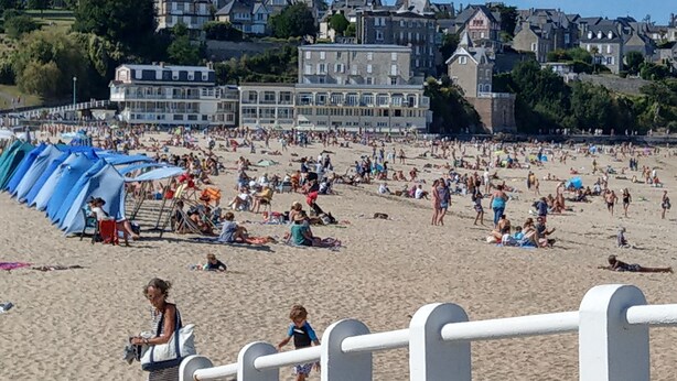 A crowded beach with people sunbathing and swimming. There are buildings in the background and a white fence in the foreground. - Bel appartement avec terrasse à 5mn de SAINT-CAST (Matignon)
