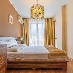 Un dormitorio con una cama de madera, una lámpara colgante, una mesita de noche y una ventana con cortinas.