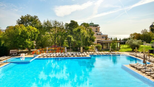 A swimming pool with lounge chairs and umbrellas, surrounded by trees and buildings. - Golden Line (Varna)