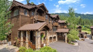 A multi-story log cabin with stone foundations, multiple balconies, and a driveway leading to a parking area.