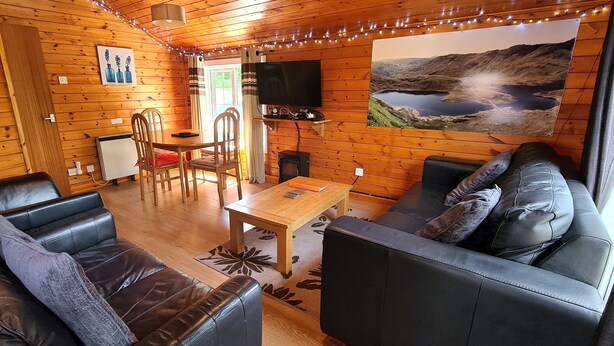 Interior acogedor de una cabaña con paredes de madera, un comedor, un sofá y un amplio ventanal con vistas panorámicas.