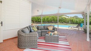 A covered outdoor area with a pool, a wicker sofa, and a striped rug.