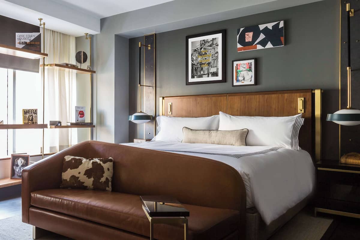 A modern hotel room with a large bed, a leather sofa, and a bedside table.