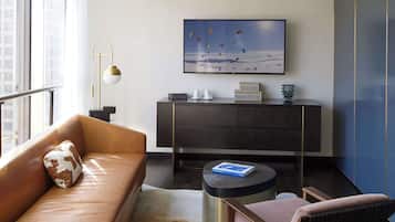 Ein modernes Wohnzimmer mit einem Ledersofa, einem Holzstuhl, einem runden Couchtisch, einer dunklen Holzkommode und einem großen Fenster.