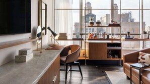 A modern living room with a large TV, a wooden coffee table, a leather sofa, and a city view through large windows. - Thompson Dallas, by Hyatt (Dallas)