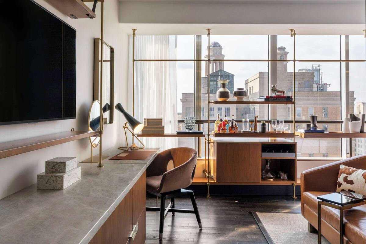 A modern living room with a large TV, a wooden coffee table, a leather sofa, and a city view through large windows.