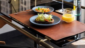 A modern dining table with a glass top, two plates of food, a glass of orange juice, a bottle of water, and a wine glass. - Thompson Dallas, by Hyatt (Dallas)