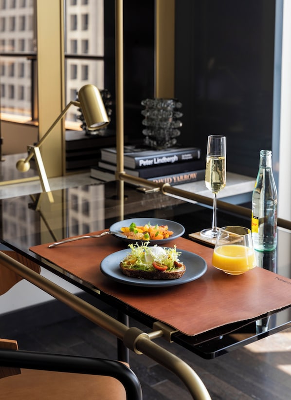 A modern dining table with a glass top, two plates of food, a glass of orange juice, a bottle of water, and a wine glass. - Thompson Dallas, by Hyatt (Dallas)