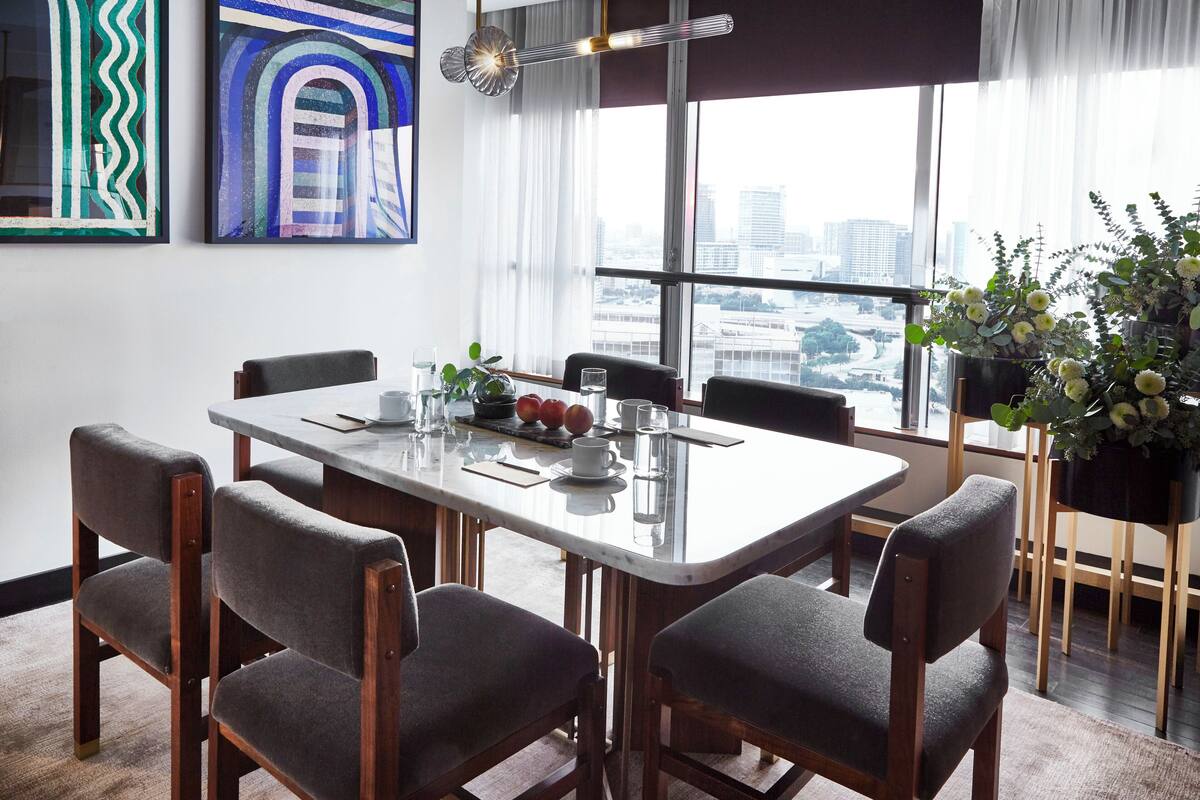 A modern dining area with a large table, six chairs, and a city view through large windows.