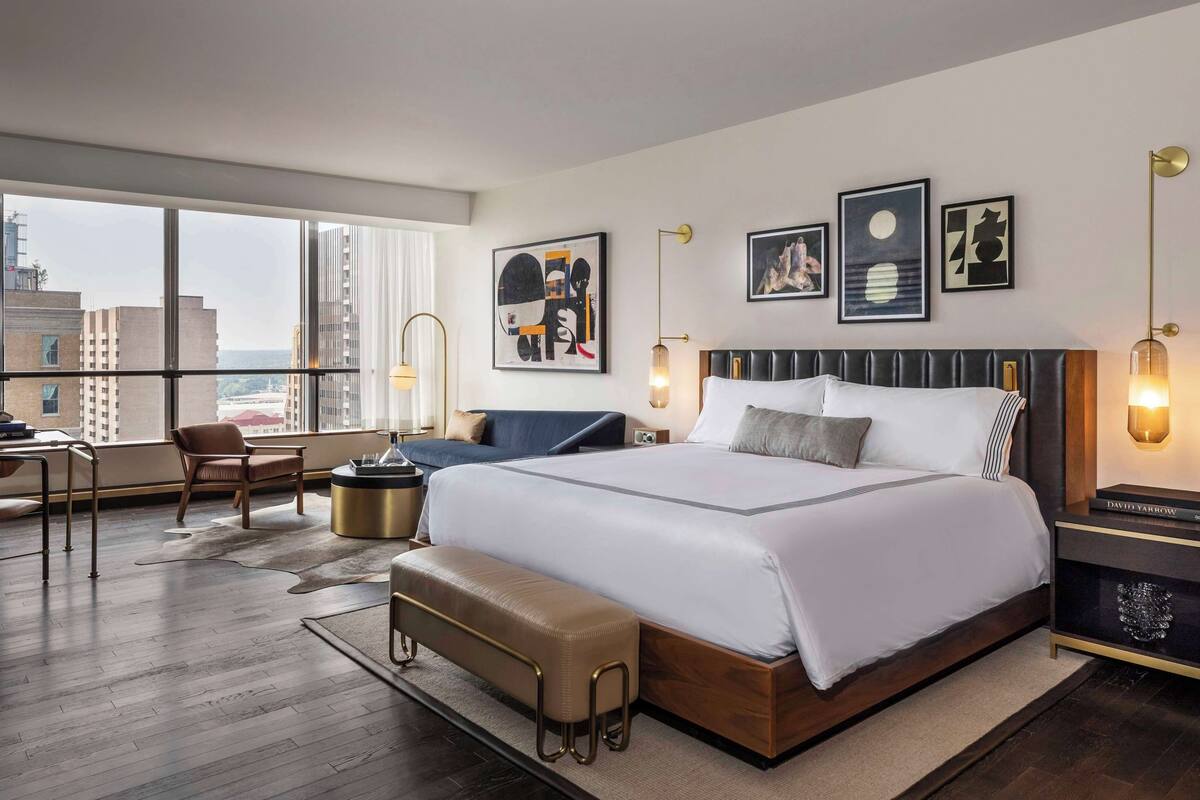 A modern hotel room with a large bed, a desk, and a view of the city.