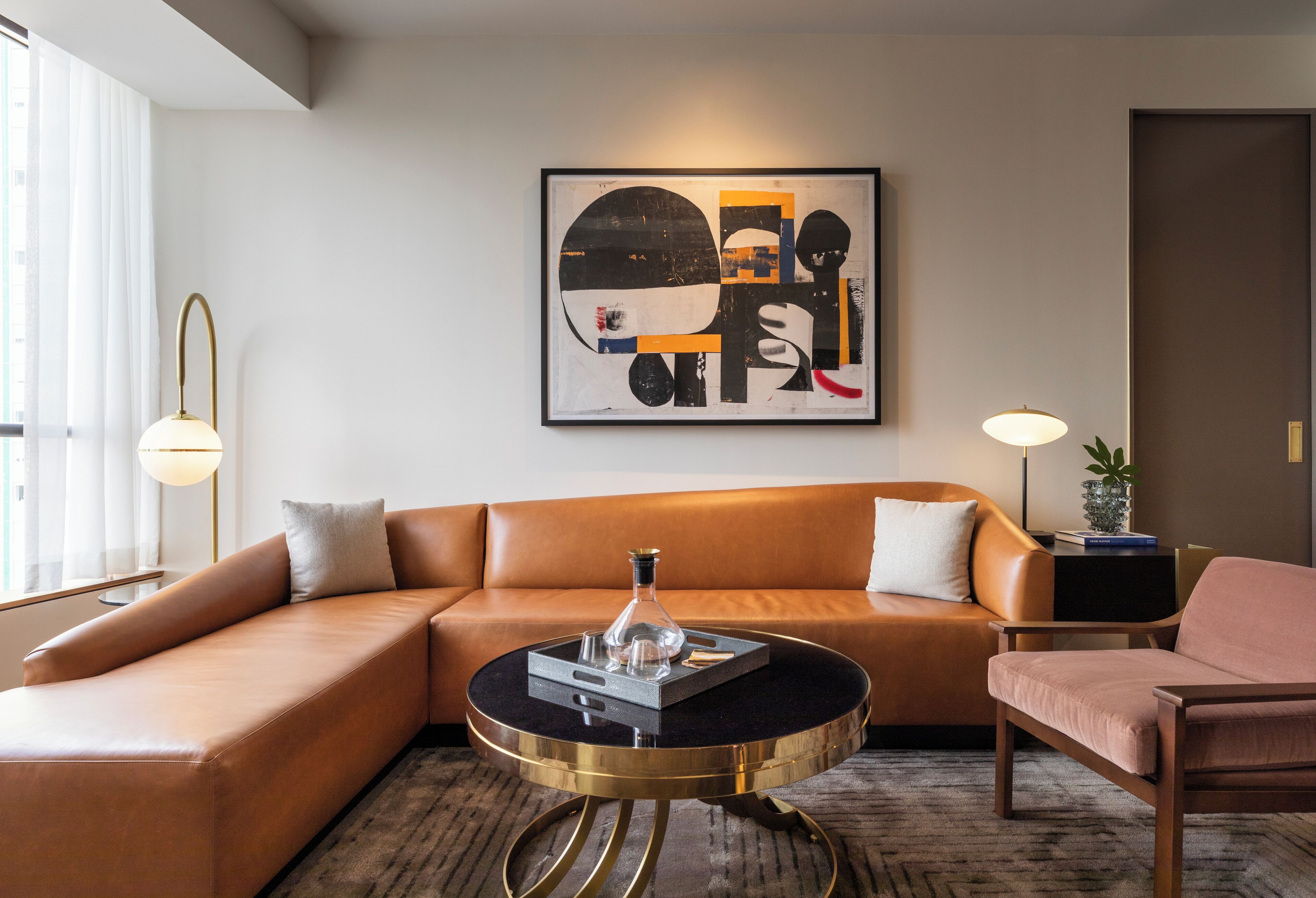 A modern living room with a brown leather sofa, a round black coffee table with gold legs, and a contemporary abstract painting on the wall.