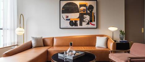 A modern living room with a brown leather sofa, a round black coffee table with gold legs, and a contemporary abstract painting on the wall.